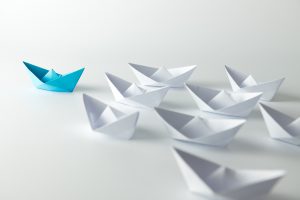 Leadership concept with blue paper ship leading among white